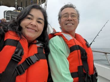 Two anglers enjoying a day on the water, wearing life jackets while seated on the boat, with fishing rods visible in the background.