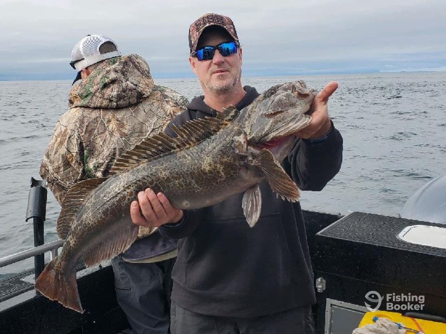 Angler proudly displaying a large Lingcod while fishing on a boat in open waters.