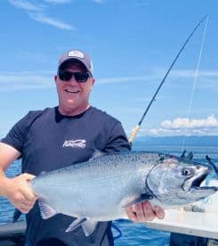 An angler proudly displaying a large Salmon while fishing on a sunny day in open waters.