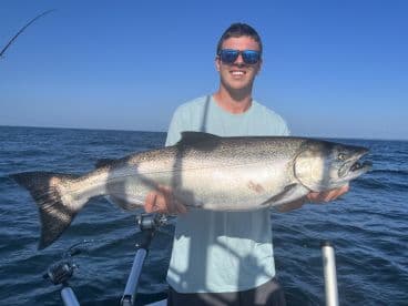 An angler proudly displaying a large Chinook Salmon while fishing offshore, showcasing a clear blue sky and calm waters.