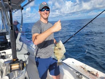 An angler reeling in a large fish while fishing on a boat in open waters, showcasing a successful catch.