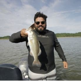 Angler proudly displaying a large Largemouth Bass while fishing on a serene lake.