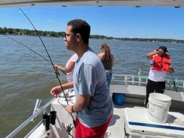 A group of anglers actively fishing on a boat, with one young angler holding a fishing rod and another preparing to reel in a catch.