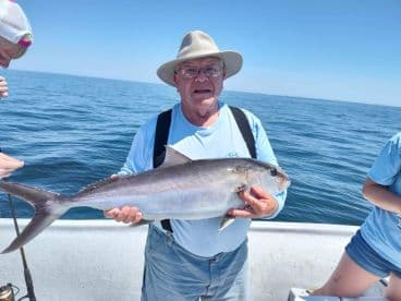 An angler proudly displaying a large Amberjack while fishing offshore, with calm waters in the background.