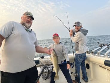 A young angler proudly displaying a large Walleye while fishing with family on a boat, showcasing a fun day on the water.