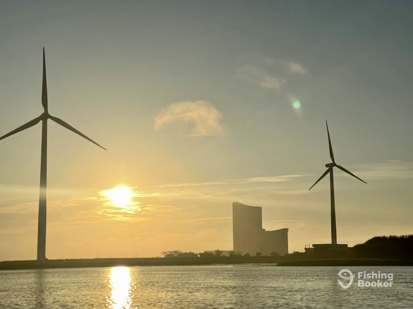 A scenic view featuring wind turbines and a sunset over the water, creating a tranquil atmosphere.