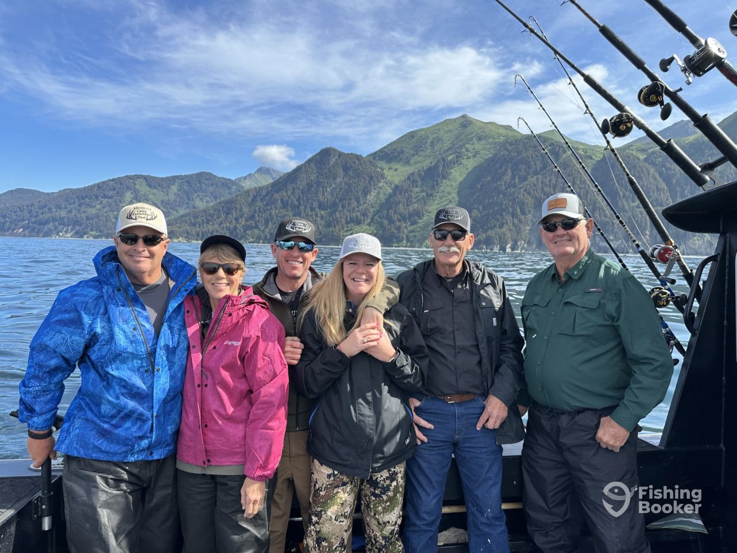 A group of six anglers posing on a fishing boat with scenic mountains in the background, showcasing a day of fishing adventure.