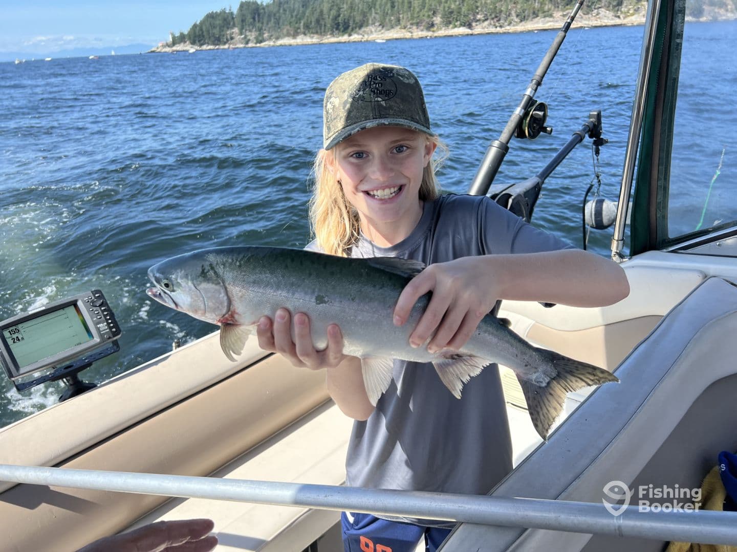 A young angler proudly displaying a caught Salmon aboard a fishing boat, enjoying a sunny day on the water.