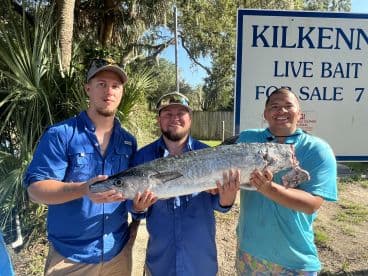Three anglers proudly displaying a large fish in front of a bait shop, showcasing their successful catch during a fishing trip.