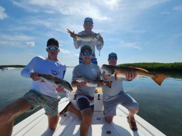 Group of anglers proudly displaying their catch of Redfish while fishing in a calm coastal environment.
