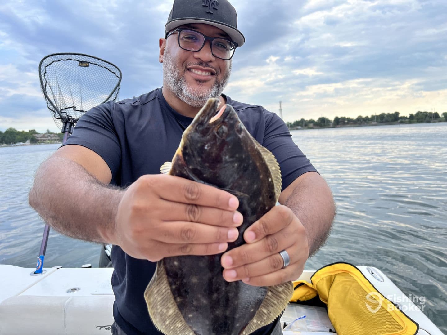 Angler proudly displaying a large Flounder while fishing on a boat, showcasing a successful day on the water.