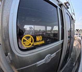 A close-up of a fishing boat's window displaying a humorous 'No Bananas' sign, emphasizing fishing superstitions. The boat is parked in a busy marina setting.