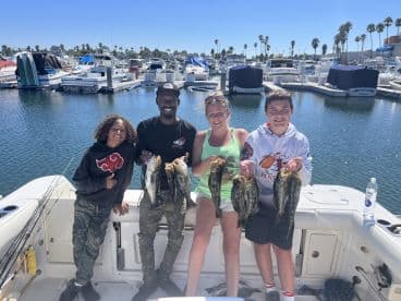 A family proudly displaying their catch of several large Bass at the marina, showcasing a successful day of fishing.