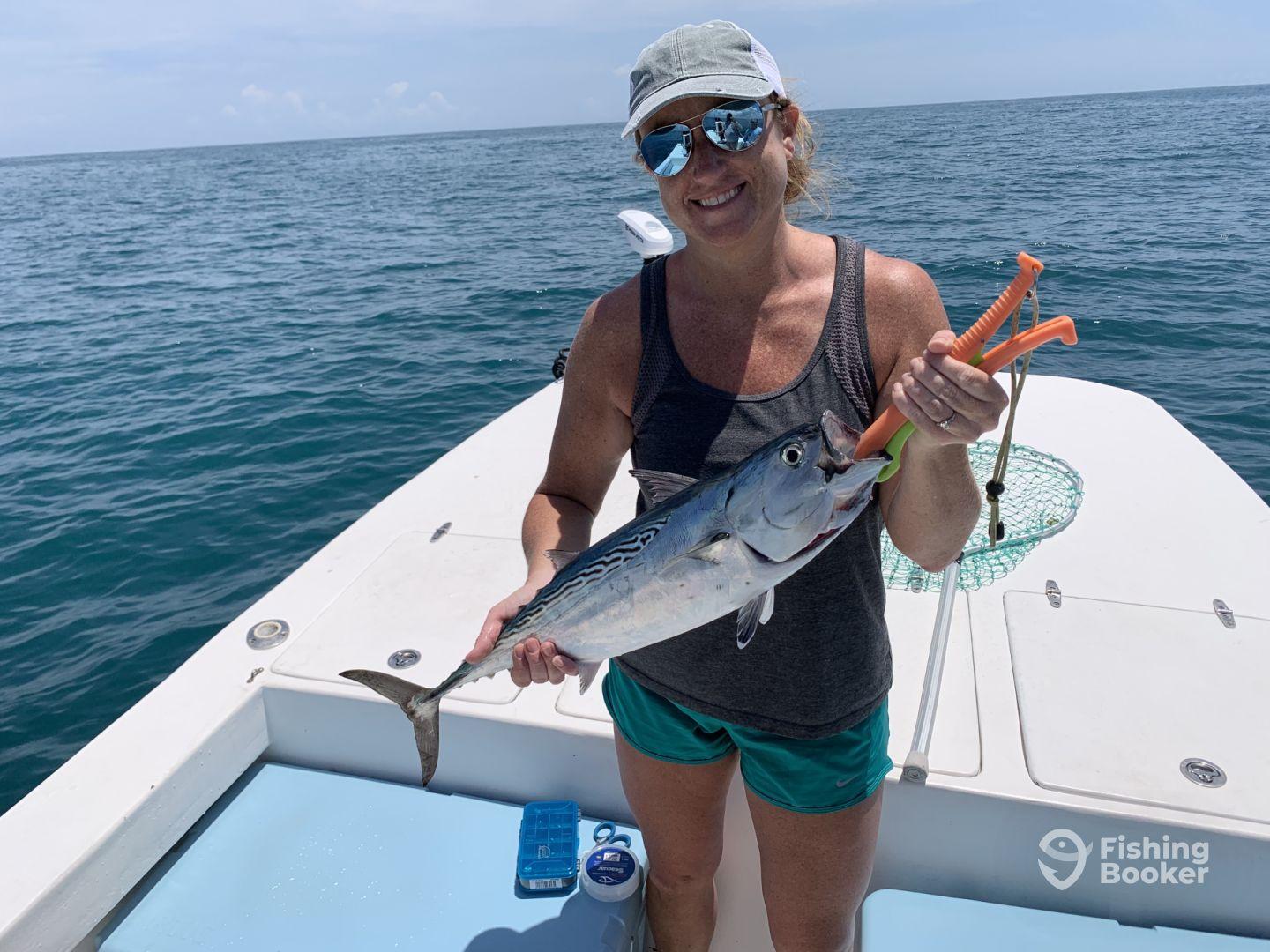 An angler proudly displaying a caught fish while aboard a boat in open waters, showcasing a sunny day fishing experience.