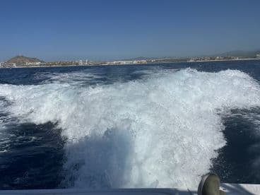 A scenic view from the boat showing the wake and coastline, highlighting the vibrant blue waters and distant land features.