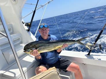 An angler proudly displaying a large Mahi Mahi while aboard a fishing boat in open waters.