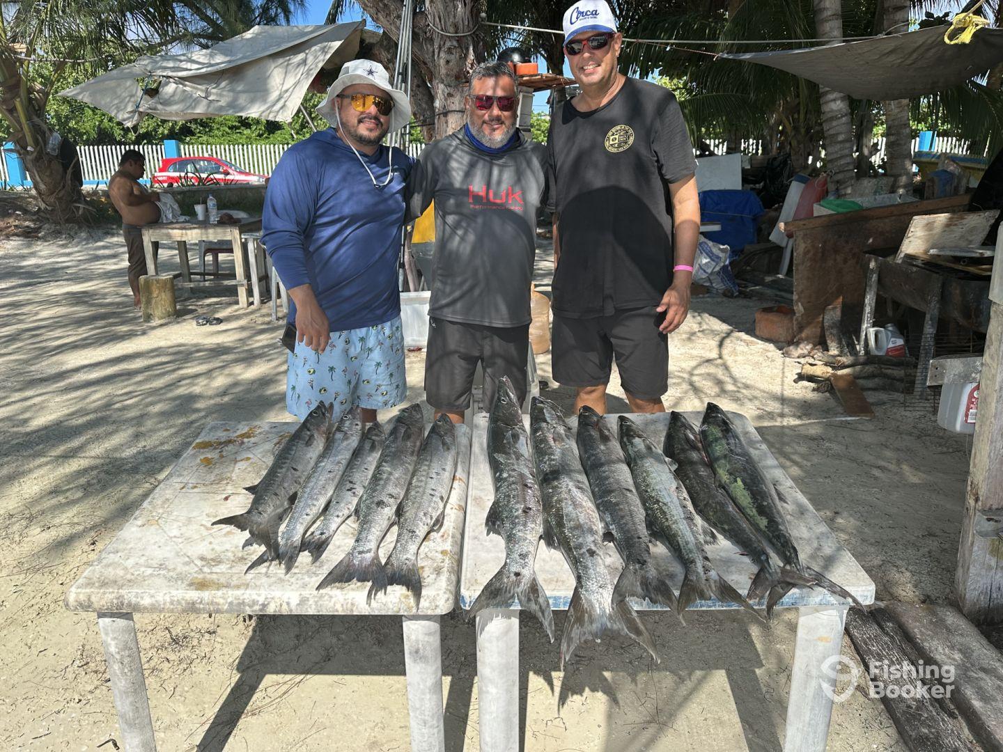 Three anglers proudly display their catch of Barracuda on a table after a successful fishing trip.