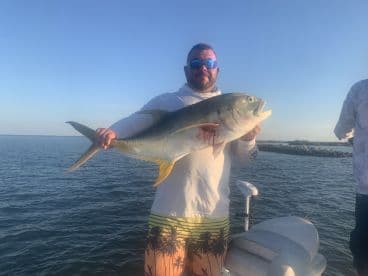 Angler proudly displaying a large Jack Crevalle while fishing on a boat in clear waters.