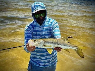 Angler displaying a large Snook while standing in shallow water, showcasing a successful day of fishing.