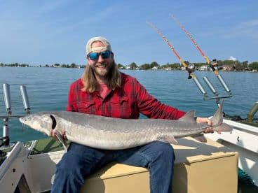 Angler proudly displaying a large Sturgeon while seated on a boat, showcasing a successful fishing trip.
