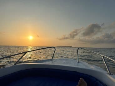 A serene sunset view from the front of a boat, showcasing the calm waters and distant land, perfect for a relaxing fishing trip.