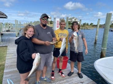 A group of young anglers proudly displaying their catch of Redfish and Speckled Trout at the dock after a successful fishing trip.