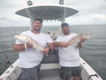 Two anglers proudly displaying their catches of Redfish while aboard a fishing boat in open waters.
