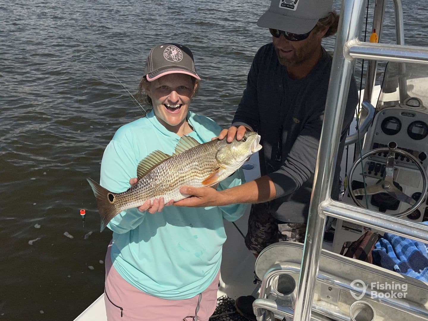 A happy angler holding a large striped bass while fishing on a boat, showcasing a successful day on the water.