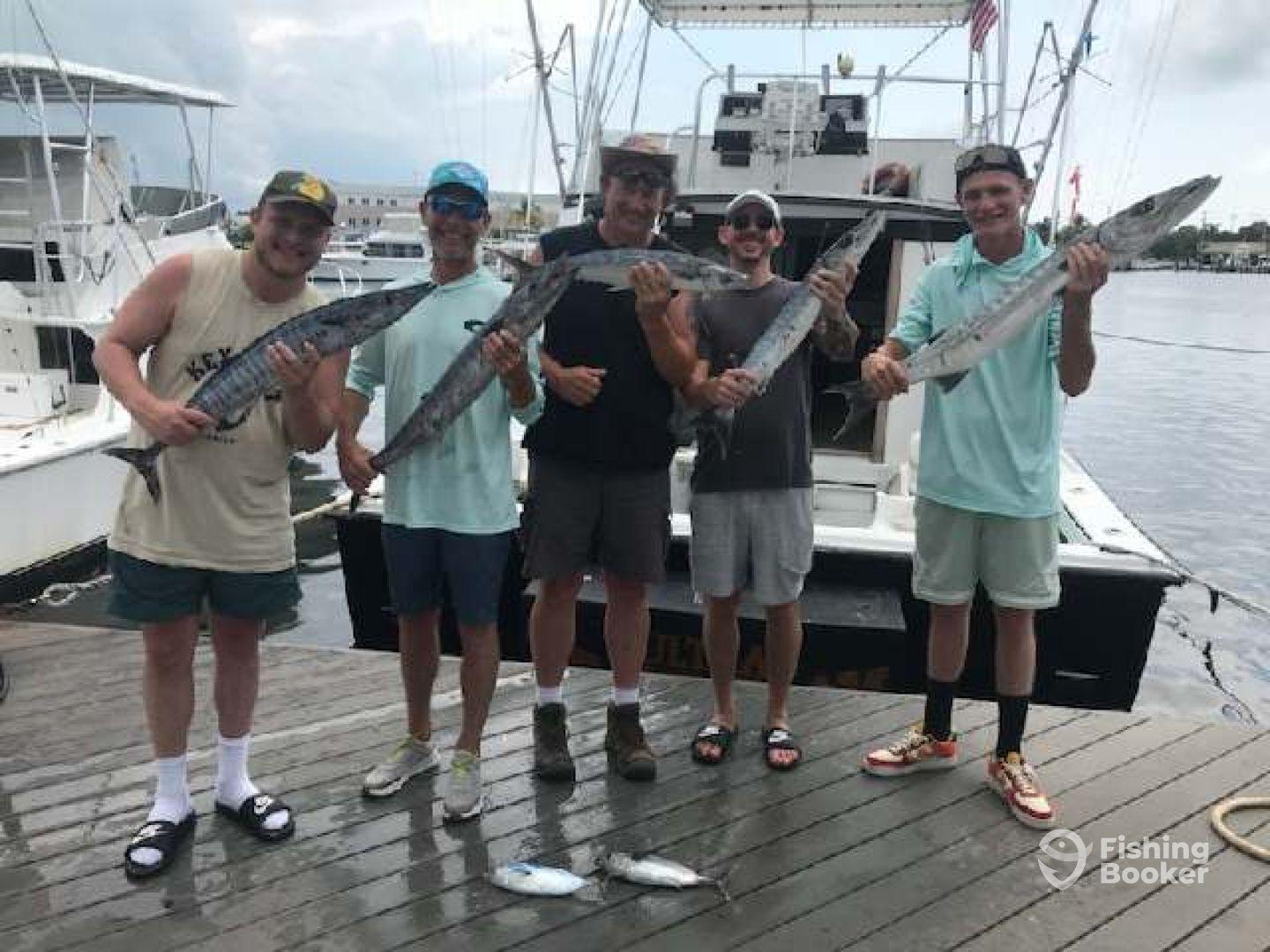Group of anglers proudly displaying their catch of Barracuda at the dock after a successful fishing trip.