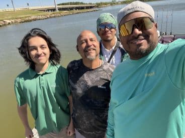 Group of four individuals posing together near the water, likely preparing for a fishing trip.