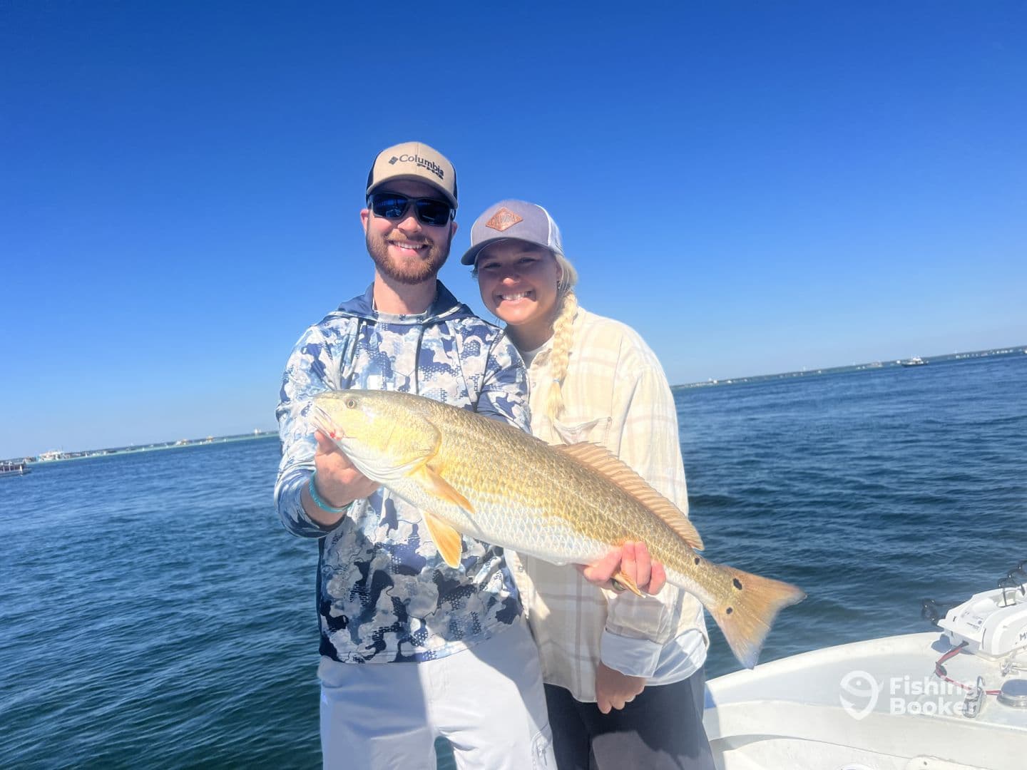 Two anglers proudly displaying a large Redfish while out on the water, showcasing a successful day of fishing.