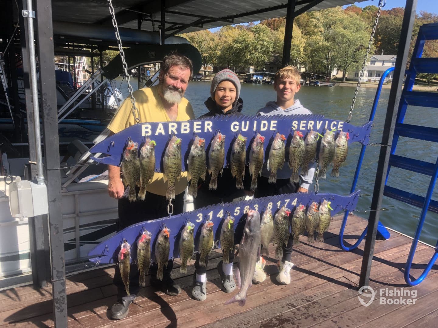 A group of anglers proudly displaying their catch of crappie and catfish on a catch board at a lakeside dock, showcasing a successful fishing trip with Barber Guide Service.