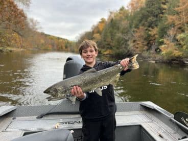 A young angler proudly displaying a large trout while fishing in a scenic river surrounded by autumn foliage.