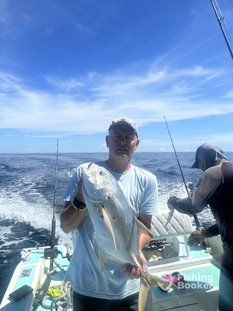 An angler proudly displaying a large Jack Crevalle while fishing on a boat in open waters.