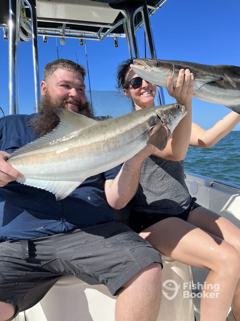 Two anglers proudly displaying their catch of large fish while enjoying a sunny day on the water.