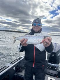 Angler proudly displaying a freshly caught fish while on a boat, surrounded by a scenic water backdrop.