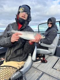 Angler displaying a freshly caught fish while seated in a boat, showcasing a relaxed fishing experience.
