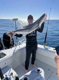 An angler proudly displaying a large Cobia aboard a fishing boat, enjoying a sunny day on the open water.