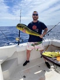An excited angler proudly displaying a vibrant Mahi Mahi aboard a fishing boat in open waters.