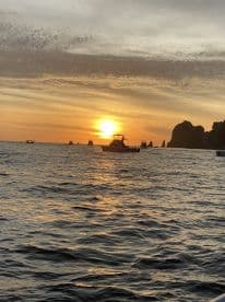 A picturesque sunset over the ocean with multiple boats silhouetted against the vibrant sky, showcasing a serene fishing environment.