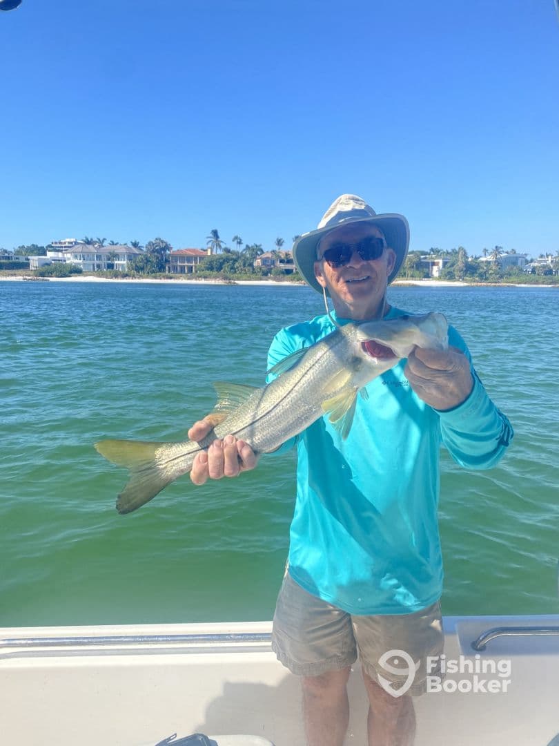 An angler proudly displaying a Snook caught while fishing from a boat in a sunny coastal environment.