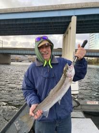 An angler proudly displaying a large Steelhead caught while fishing under a bridge, showcasing a successful day on the water.