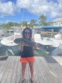 An adult angler proudly displaying a large Mahi-Mahi at the dock, surrounded by boats in a tropical fishing environment.