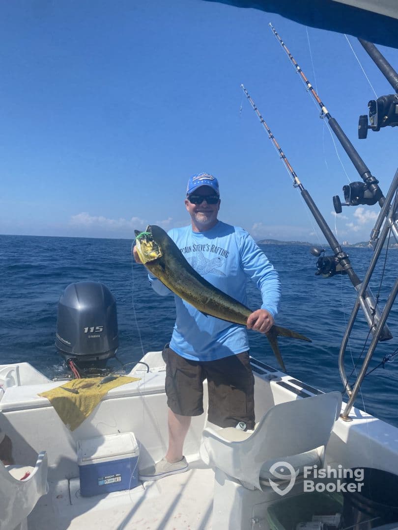 An angler proudly displaying a vibrant Mahi Mahi aboard a fishing boat, enjoying a sunny day on the open water.