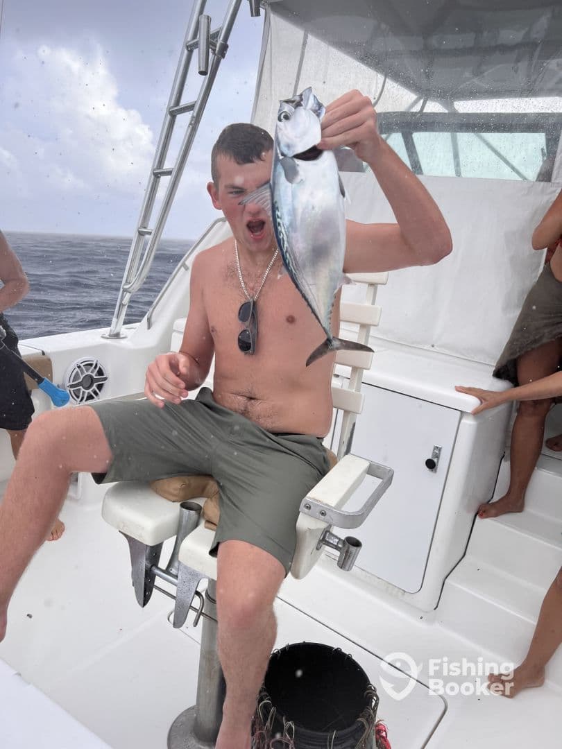 A young angler excitedly holds up a freshly caught fish while seated on a fishing boat, showcasing the thrill of deep-sea fishing.