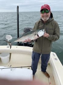 An angler proudly displaying a large Spanish Mackerel while fishing on a boat in open waters.