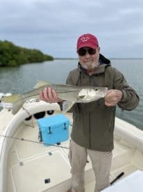 An angler proudly displaying a Snook caught while fishing from a boat in a coastal waterway.