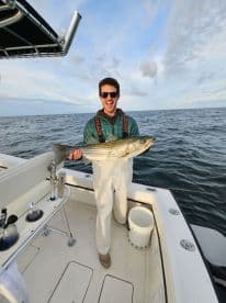Angler celebrating with a large Striped Bass aboard a fishing boat, showcasing a successful day on the water.