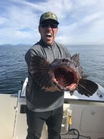 An enthusiastic angler proudly displaying a large Lingcod while fishing offshore, showcasing the excitement of a successful catch.
