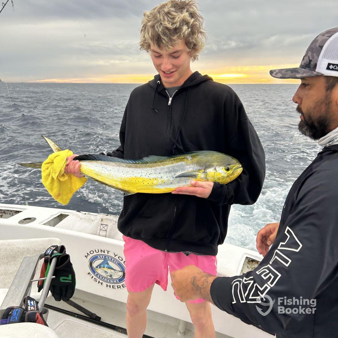 A young angler proudly displaying a vibrant Mahi Mahi while fishing on a charter boat, with a scenic ocean backdrop.